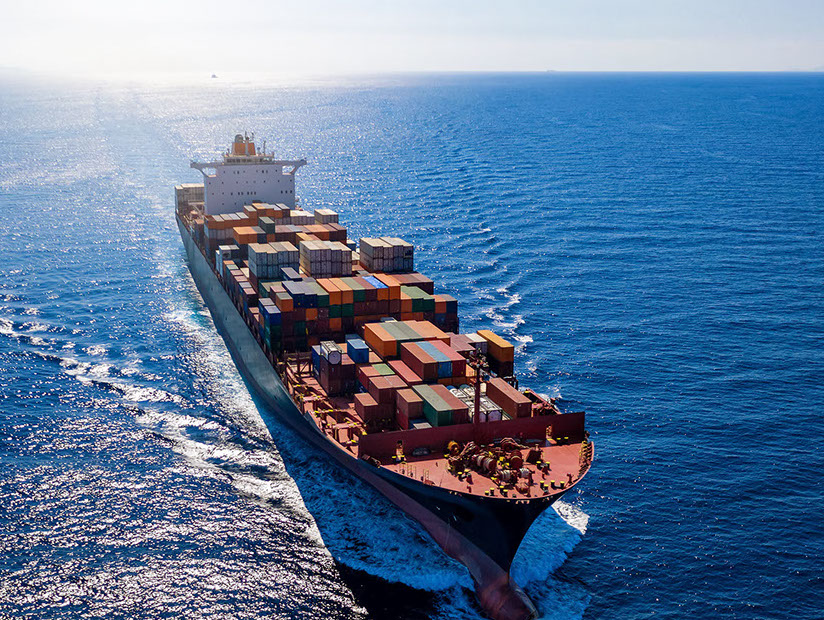 Luftaufnahme ein beladenen Containerschiffes bei voller Fahrt über blauem Meer